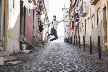 Unbekümmerter junger Mann beim Springen in der Altstadt, Lissabon, Portugal - UUF20368