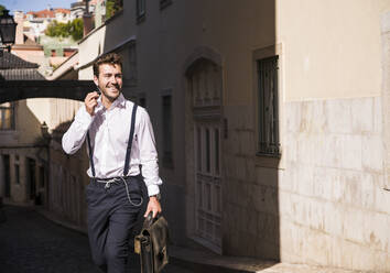Smiling young man with earbuds in the old town, Lisbon, Portugal - UUF20369