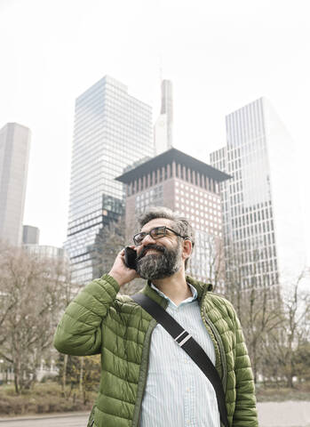 Mann am Telefon vor Wolkenkratzern, Frankfurt, Deutschland, lizenzfreies Stockfoto