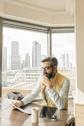 Mann bei der Arbeit in einem Café mit Blick auf Wolkenkratzer, Frankfurt, Deutschland - AHSF02464