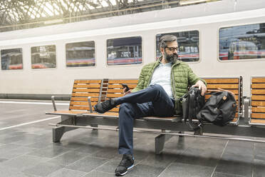 Mann sitzt auf einer Bank am Bahnhof - AHSF02476