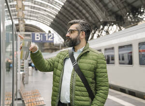 Mann bei der Fahrplankontrolle am Bahnhof - AHSF02479