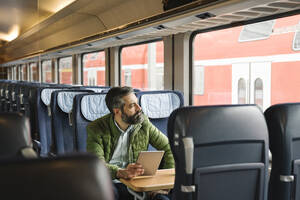 Mann sitzt im Zug und hält ein Tablet - AHSF02483