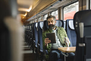 Mann sitzt im Zug und benutzt ein Tablet - AHSF02484