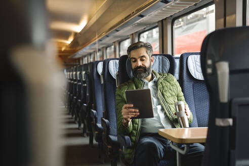 Mann sitzt im Zug und benutzt ein Tablet - AHSF02484