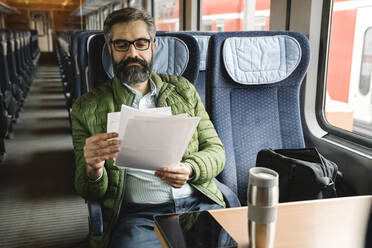 Mann sitzt im Zug und liest Dokumente - AHSF02485