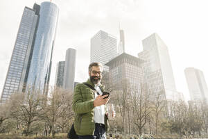Mann mit Smartphone vor Wolkenkratzern, Frankfurt, Deutschland - AHSF02493