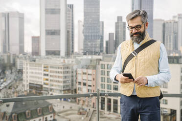 Mann mit Smartphone vor Wolkenkratzern, Frankfurt, Deutschland - AHSF02509