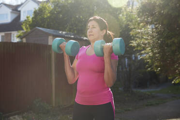 Dedicated woman lifting dumbbells while exercising at back yard - PMF01032