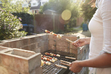 Midsection von Frau Kochen von Lebensmitteln mit Spießen auf dem Grill im Hinterhof während sonnigen Tag - PMF01046