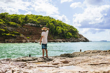 Rückenansicht eines Mannes, der auf einer Klippe steht und aufs Meer schaut, Cala Benirras, Ibiza, Spanien - KIJF02994
