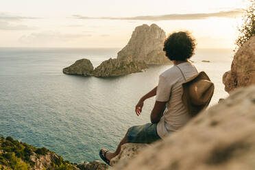 Mann sitzt auf einem Felsen und beobachtet den Sonnenuntergang, Ibiza, Spanien - KIJF02995