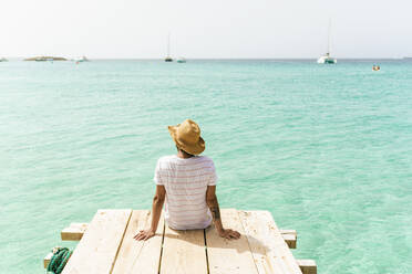Rückenansicht eines Mannes, der auf einem Holzsteg sitzt und auf das Meer schaut, Formentera, Spanien - KIJF03000