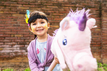 Portrait of girl with braids and feather headdress riding a pink unicorn - GEMF03639