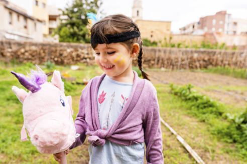 Porträt eines Mädchens mit Zöpfen und Federkopfschmuck mit einem rosa Einhorn - GEMF03641