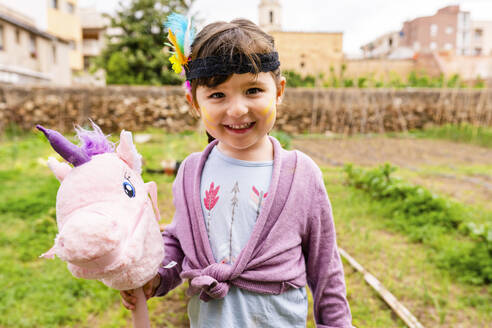 Porträt eines Mädchens mit Zöpfen und Federkopfschmuck mit einem rosa Einhorn - GEMF03642