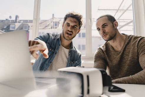Zwei junge Geschäftsleute betrachten einen Laptop mit VR-Brille auf dem Schreibtisch - KNSF08021