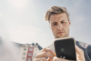 Young man using smartphone on the bacony - KNSF08053