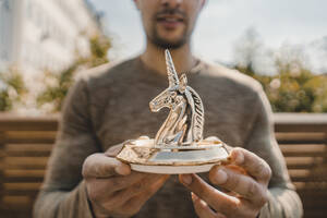 Young entrepreneur holding unicorn figurine, close up - KNSF08058