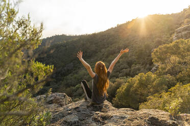 Back view of happy young woman sitting on rock in the mountains at sunset - AFVF06205