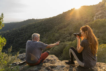 Young woman taking photo of her father in the mountains at sunset - AFVF06208