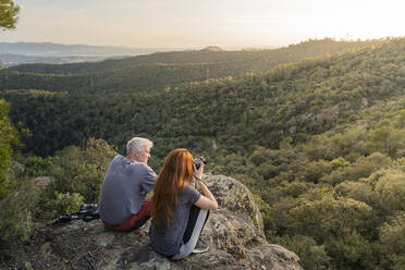 Father and adult daughter sitting on rock enjoying view at sunset - AFVF06209