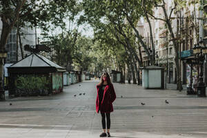 Full length portrait of woman standing on empty footpath in city, Barcelona, Spain - GMLF00179