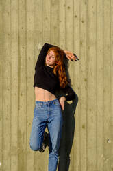 Portrait of smiling teenage girl with eyes closed leaning against concrete wall enjoying sunlight - LBF03057