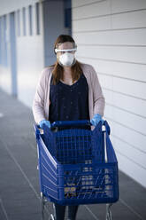 Woman walking while pushing shopping cart outside supermarket during COVID-19 pandemic - SNF00003