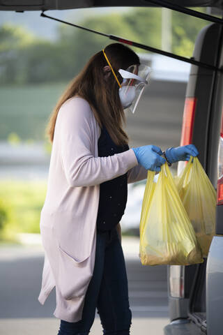 Side view of customer holding plastic bags by vehicle trunk at supermarket parking lot stock photo