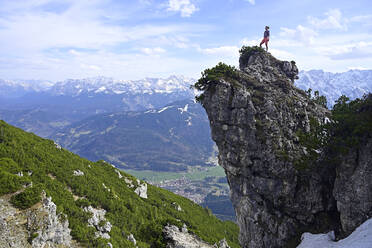 Wanderin steht auf einem felsigen Berggipfel und betrachtet die Landschaft gegen den Himmel - ECPF00901