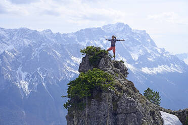 Frau steht mit ausgestreckten Armen auf einem felsigen Berggipfel und betrachtet die Landschaft gegen den Himmel - ECPF00904