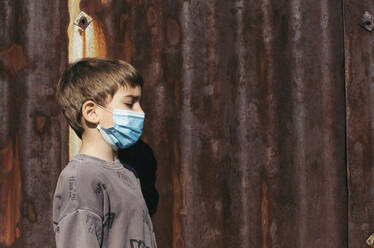 Profil eines Jungen mit Schutzmaske vor einer rostigen Mauer - MOMF00866