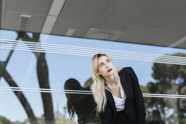 Porträt einer jungen Geschäftsfrau mit gefärbtem blondem Haar vor einem Bürogebäude mit Blick in die Ferne - TCEF00568