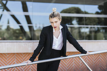 Portrait of young businesswoman wearing black pantsuit standing in front of an office building - TCEF00577
