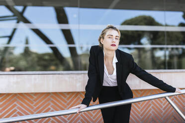 Portrait of young businesswoman wearing black pantsuit standing in front of an office building - TCEF00578