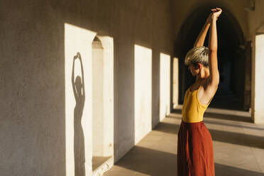 Portrait of blond female teenager with raised arms looking on her shadow on the wall - TCEF00587