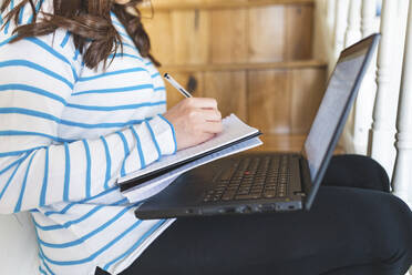 Frau mit Laptop, schreibt in Notizbuch - WPEF02865