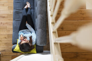 Woman phoning and sitting on sofa at home, from above - WPEF02873