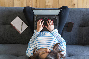 Frau zu Hause auf dem Sofa sitzend und mit Laptop arbeitend, von oben - WPEF02875