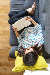 Frau entspannt sich auf dem Sofa und liest ein Buch - WPEF02877