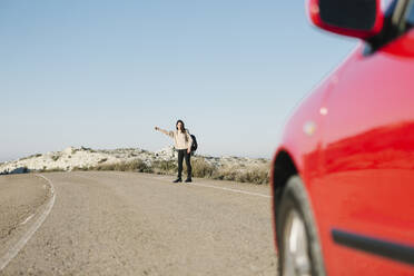 Full length of woman hitchhiking on roadside at desert against clear blue sky - XLGF00129