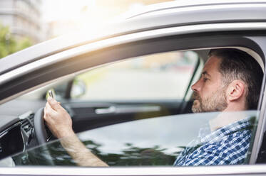 Seitenansicht eines gut aussehenden Mannes, der im Auto sitzend ein Mobiltelefon benutzt - DIGF10260