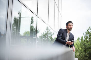 Thoughtful businessman leaning on railing while looking away from office balcony - DIGF10269