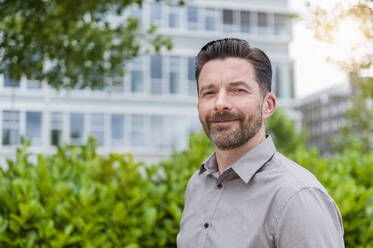 Portrait of smiling handsome bearded businessman in financial district - DIGF10281