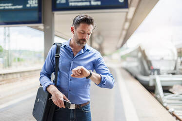 Bärtiger Pendler schaut auf seine Armbanduhr, während er auf dem Bahnsteig steht - DIGF10287