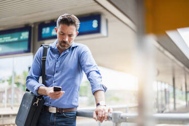 Mature businessman using smart phone while waiting at railroad station - DIGF10288