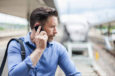 Gutaussehender Geschäftsmann, der am Bahnhof mit seinem Smartphone telefoniert - DIGF10289