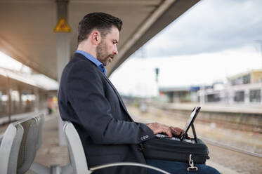 Seitenansicht eines selbstbewussten reifen Geschäftsmannes, der an einem digitalen Tablet arbeitet, während er am Bahnhof wartet - DIGF10291