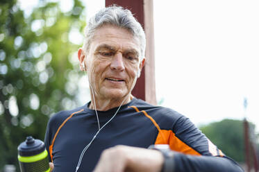 Senior man checking time while walking at park - DIGF10301